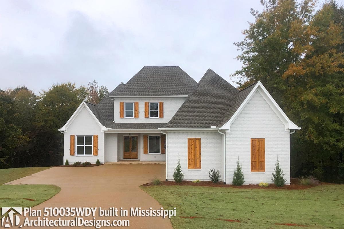 House plan exterior with brick facade, gables, dormers, and wood shutters. Two stories with a prominent roofline.