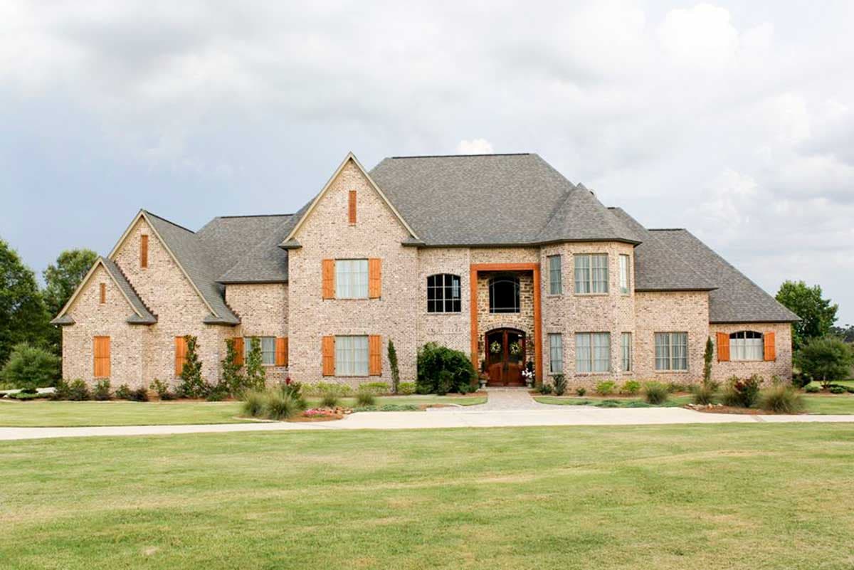 House plan exterior with multi-gabled roof, brick facade, and multiple dormers. Features include a prominent entry and shuttered windows.