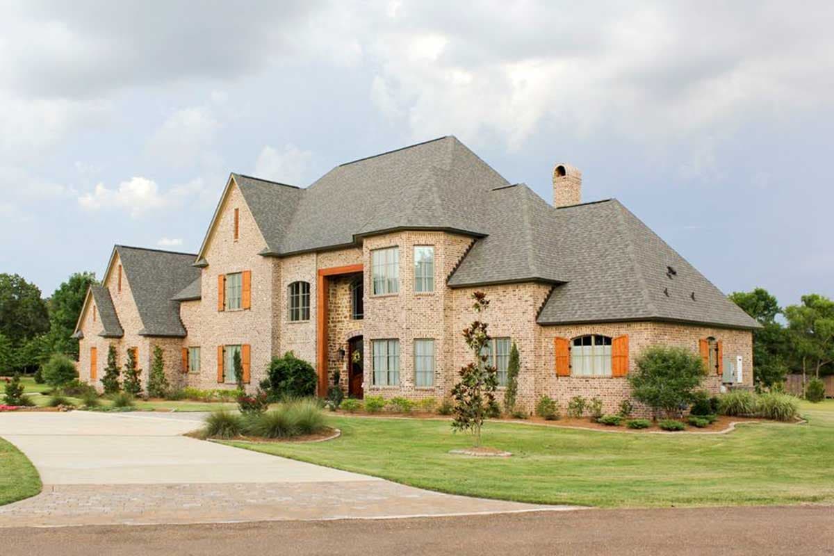 House plan exterior of a two-story brick home with multiple gables, arched windows, and orange shutters.