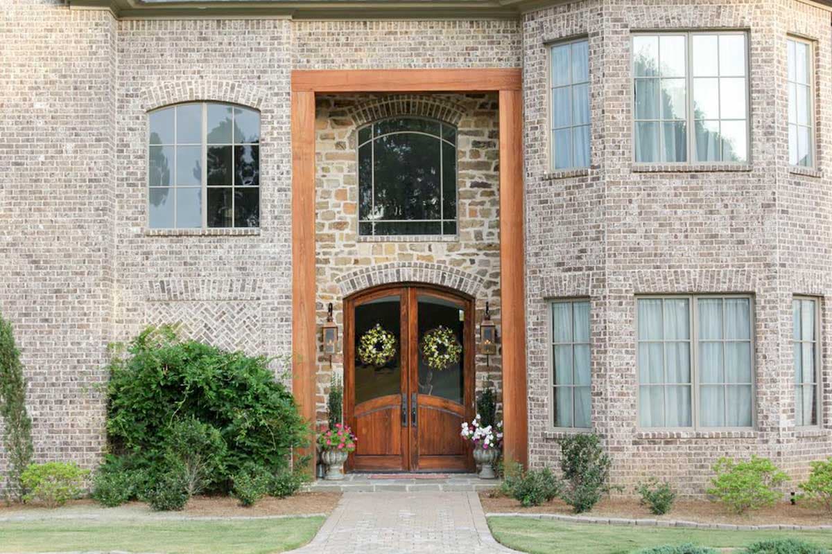 House plan exterior with brick facade, arched windows, wood-framed entry, and double wooden doors.