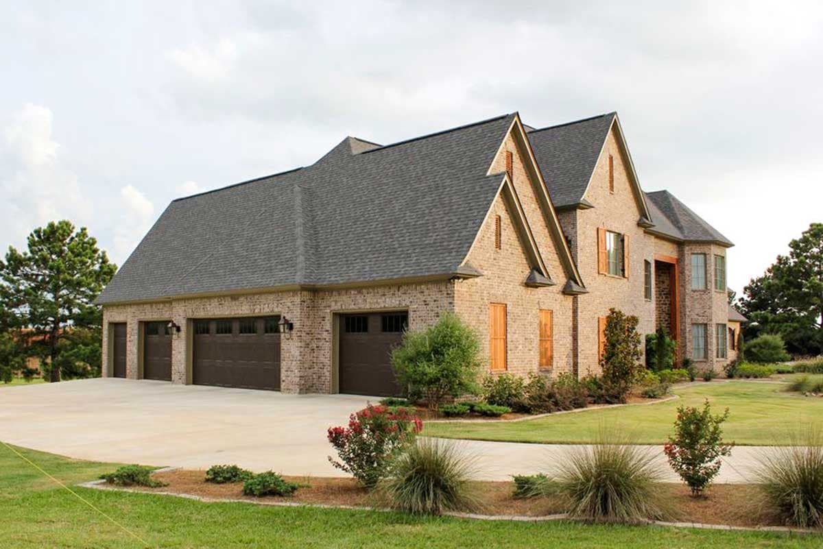 House plan exterior: Brick two-story home with a three-car garage, prominent gables, and bay windows.