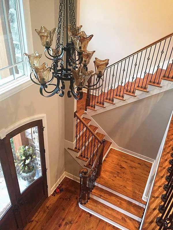Interior view of a grand staircase with wooden treads, wrought iron balusters, and a large chandelier.