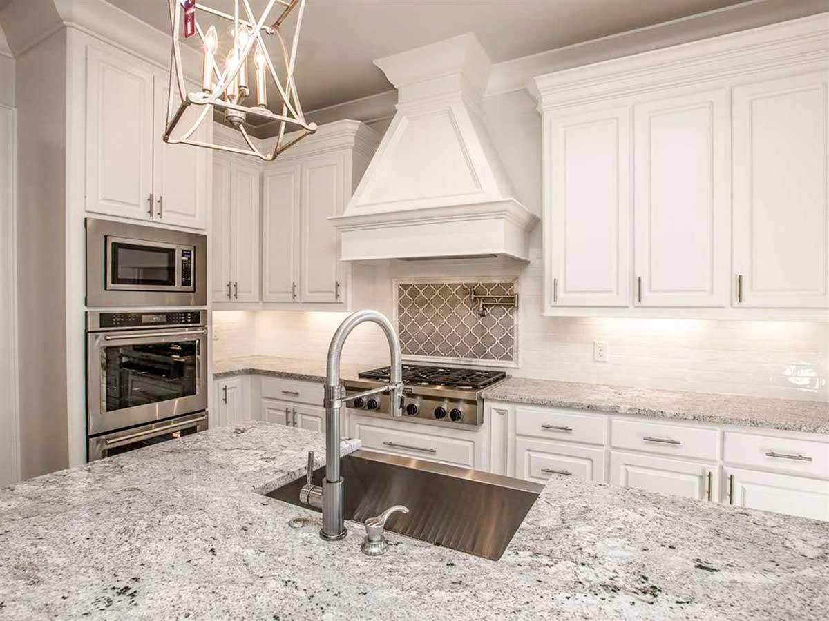 Kitchen with white cabinets, built-in ovens, gas range, island sink, and granite countertops.