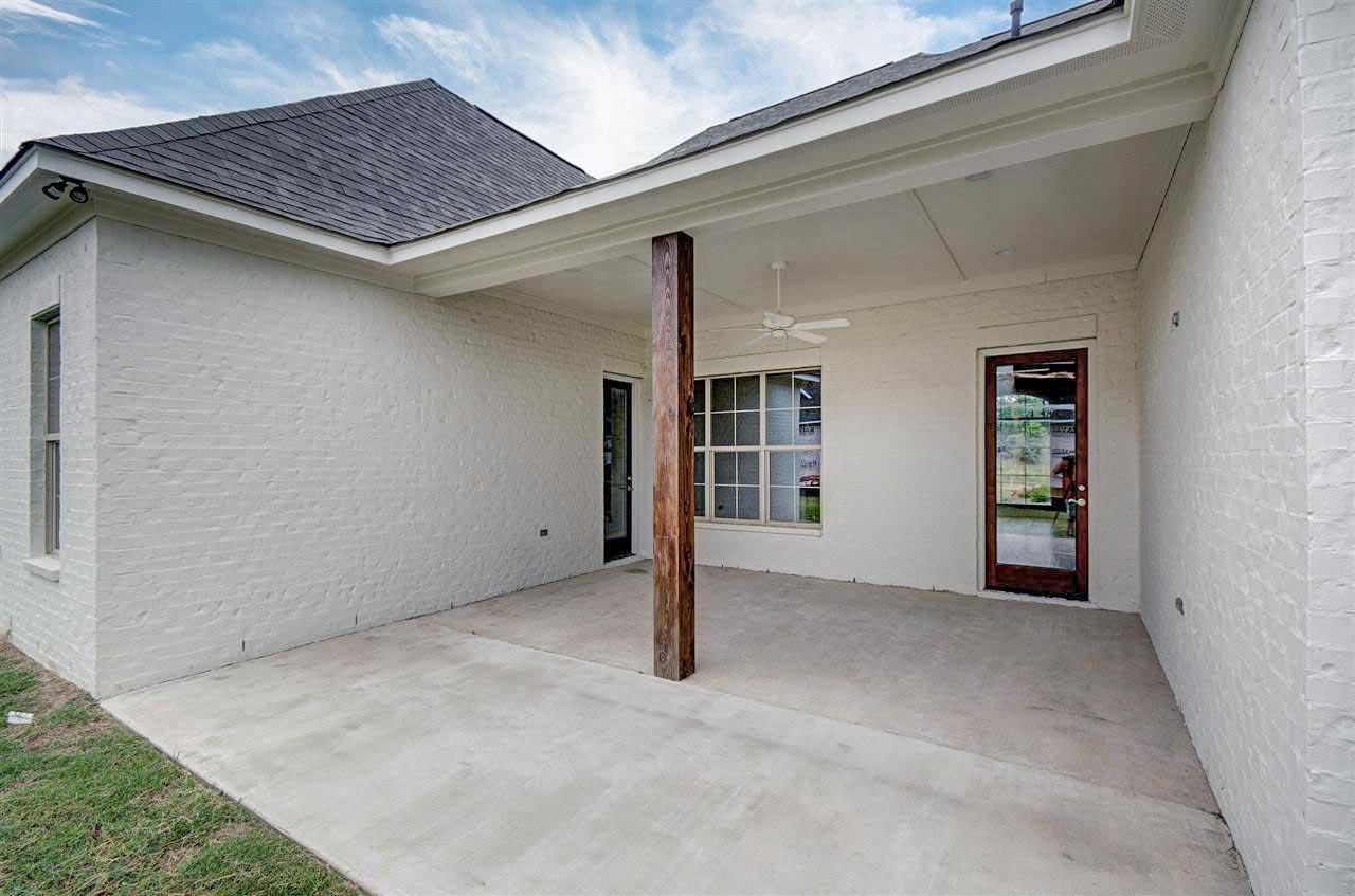 House plan exterior featuring a covered patio with a wooden post, white brick walls, and glass doors.