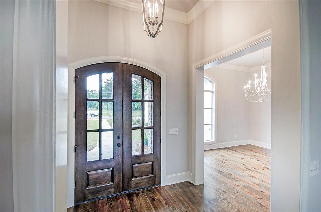 Interior view: Double wood doors with glass panes, arched transom, and foyer chandelier leading to a room with arched windows.