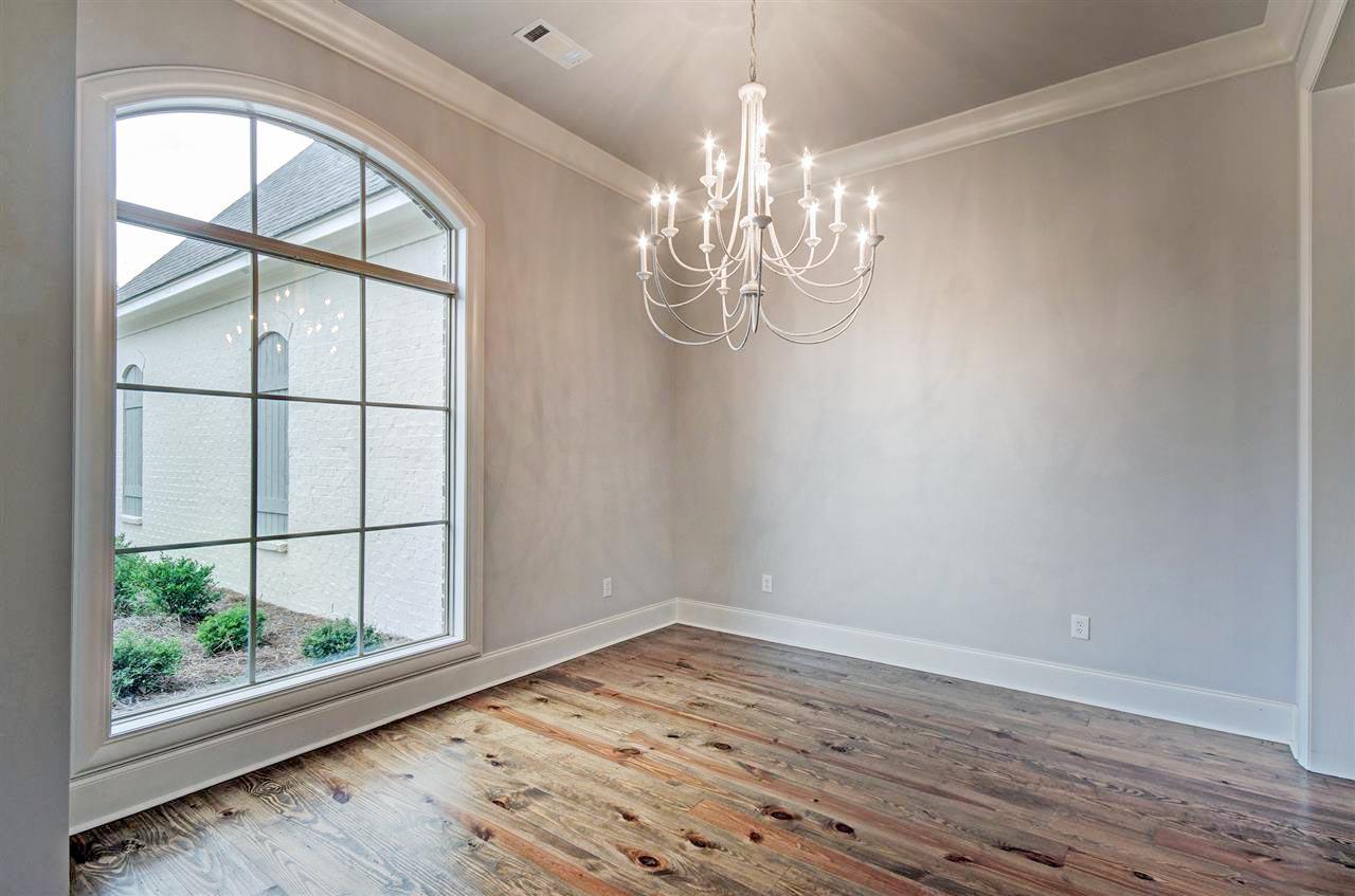 Interior view of room with large arched window, distressed wood floors, and ornate chandelier.