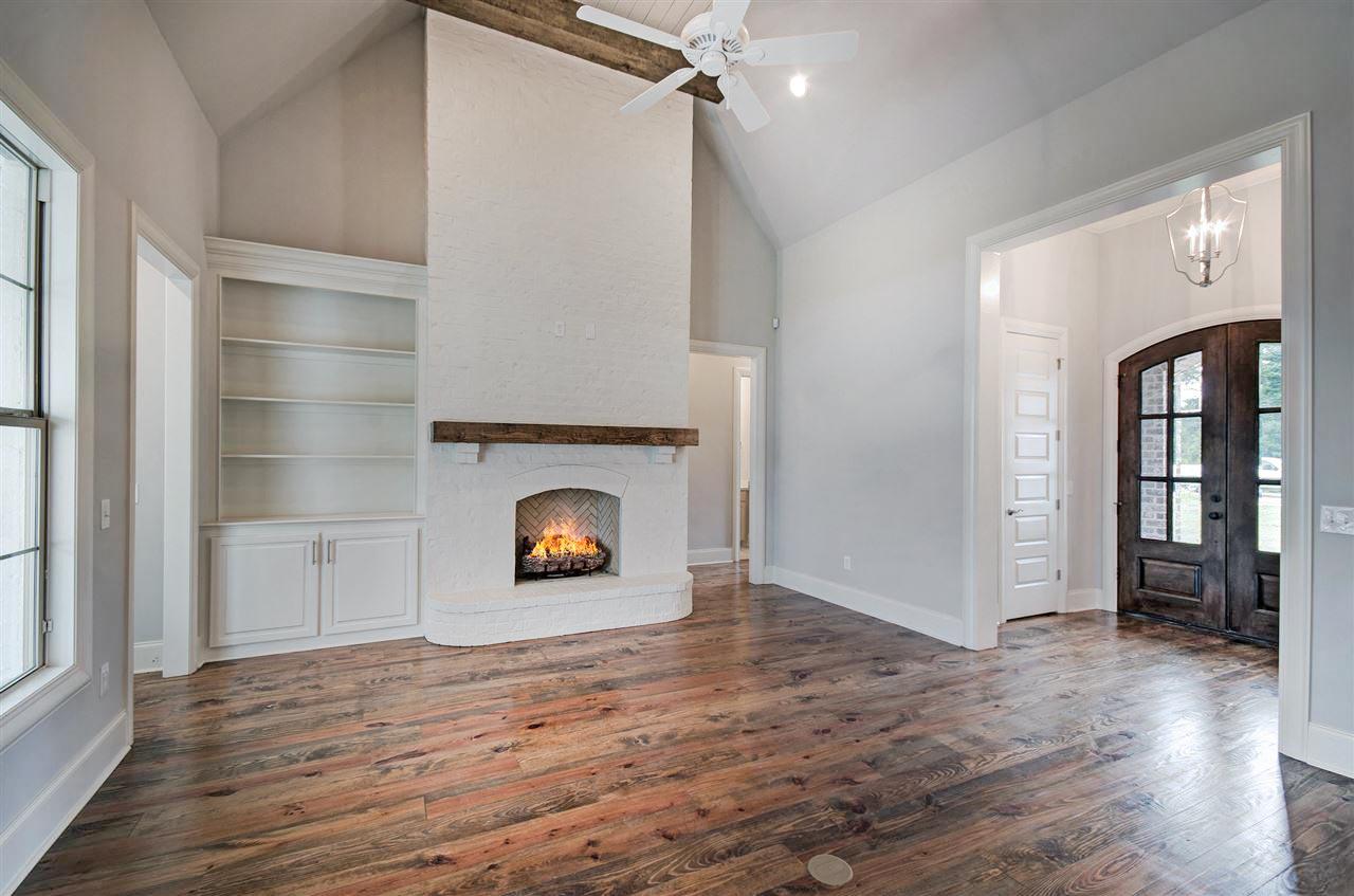 Great room with vaulted ceiling, white brick fireplace, built-in shelves, and double wood doors. Flooring is distressed wood.