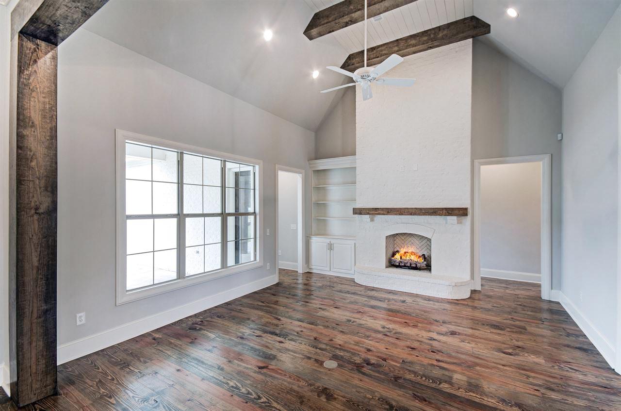 Living room with vaulted ceiling, exposed beams, fireplace, built-in shelving, and large grid window.
