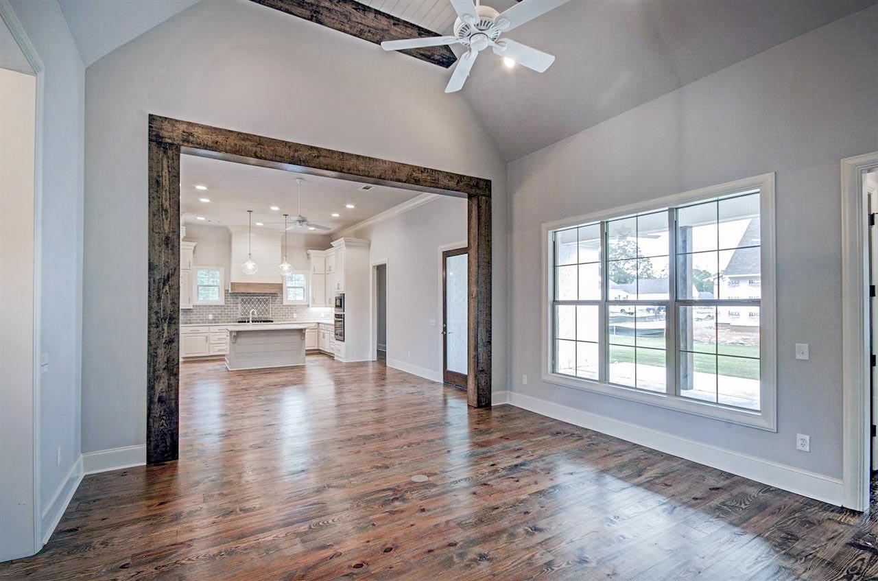 Interior view of living room with vaulted ceiling, exposed beams, and large window overlooking the kitchen area with island.