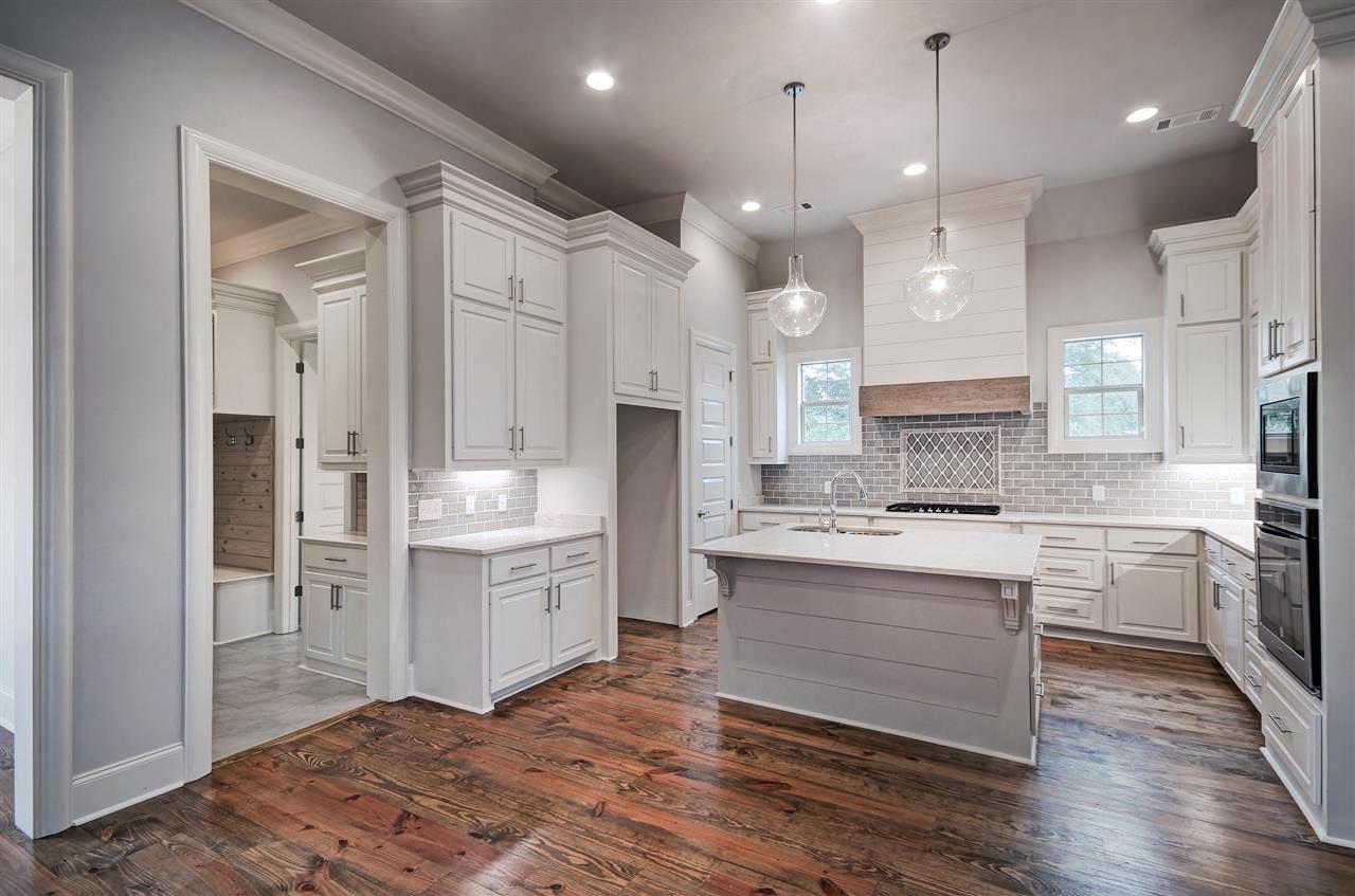 Kitchen with island, white cabinets, gray subway tile backsplash, wood range hood, and wood plank flooring.