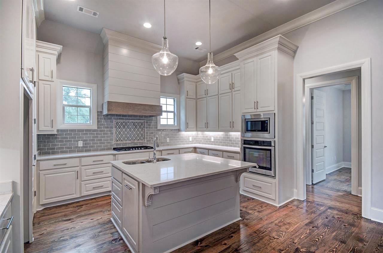 Kitchen with white cabinets, a gray subway tile backsplash, island with sink, and stainless steel appliances.