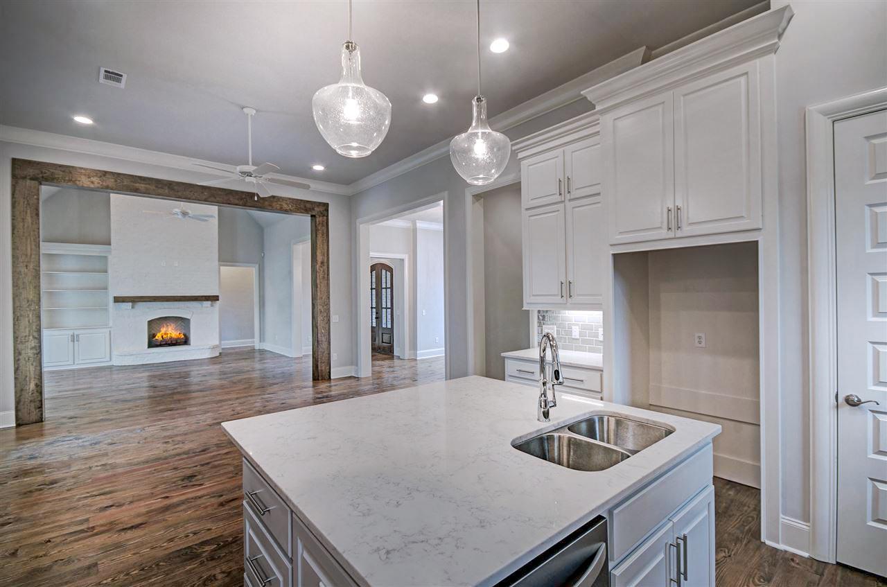 Interior view of a kitchen with island sink and white cabinetry, opening to a living room with fireplace and built-in shelving.