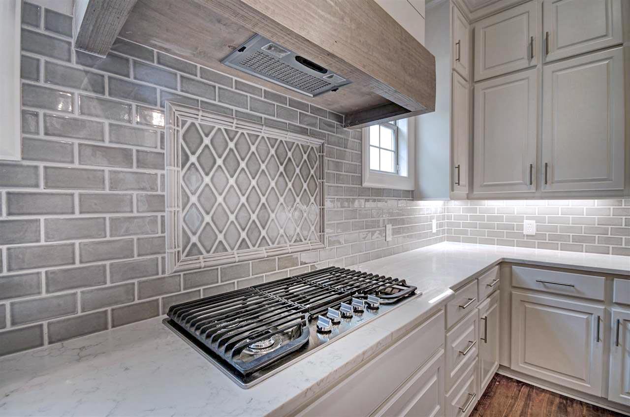 Kitchen area with subway tile backsplash, decorative tile accent, range hood, and white cabinetry.