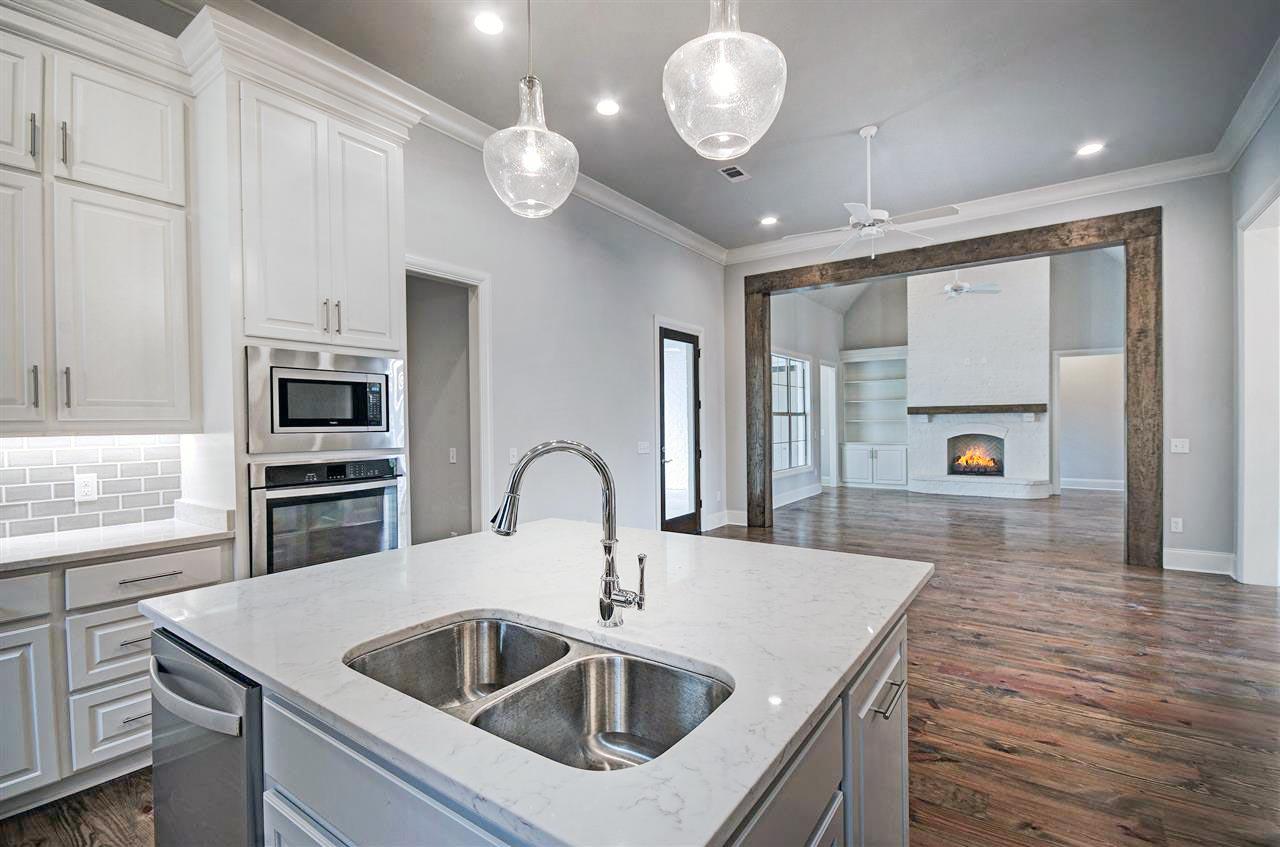 Kitchen island with sink, stainless steel appliances, and view of living room with fireplace and built-in shelves.