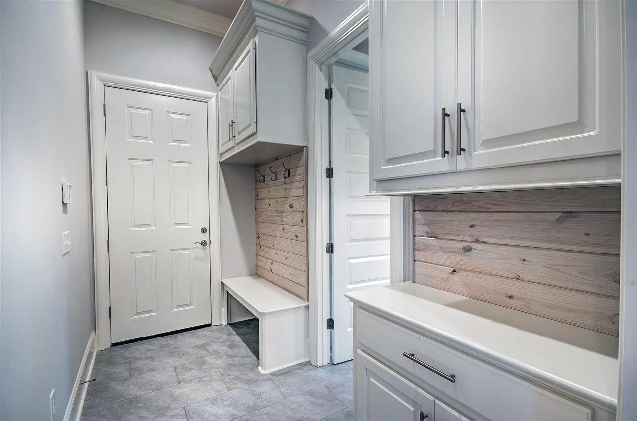 Interior view of a mudroom featuring white cabinetry, a bench with hooks, shiplap accents, and tile flooring.