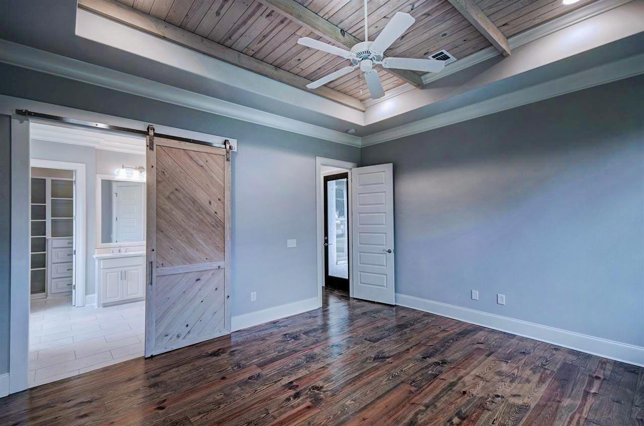 Interior view of bedroom with wood plank ceiling, barn door, and view into bathroom with vanity and closet.