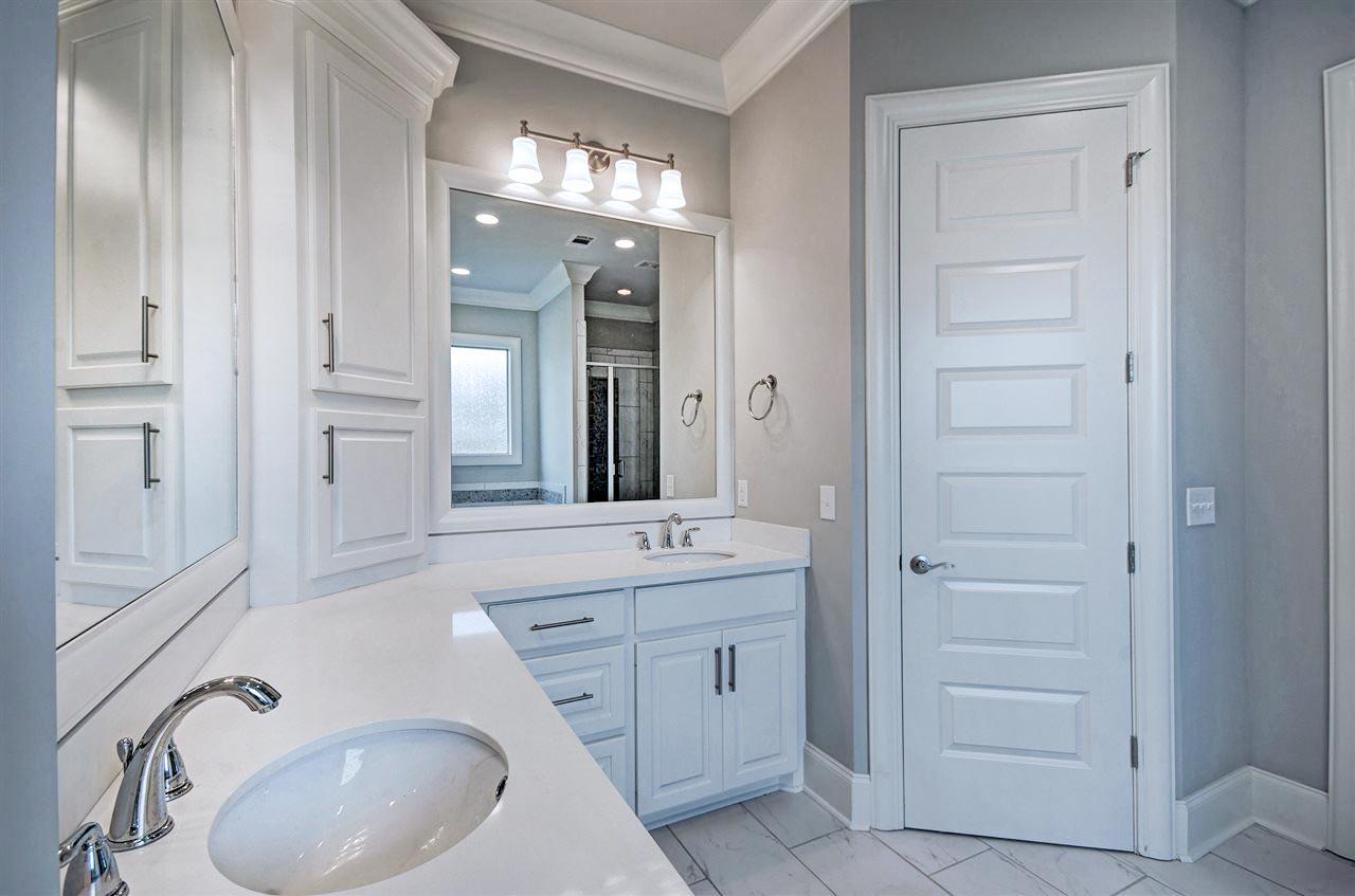 Bathroom vanity with double sinks, white cabinetry, and a large mirror. A modern five-panel door is visible.