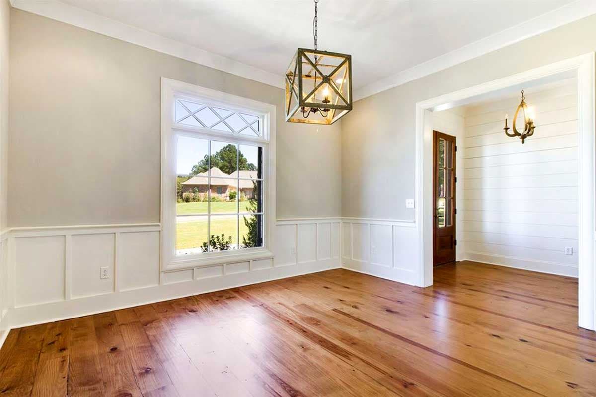 Interior view of a room with wainscoting, a large grid window, and hardwood floors. A modern lantern hangs from the ceiling.