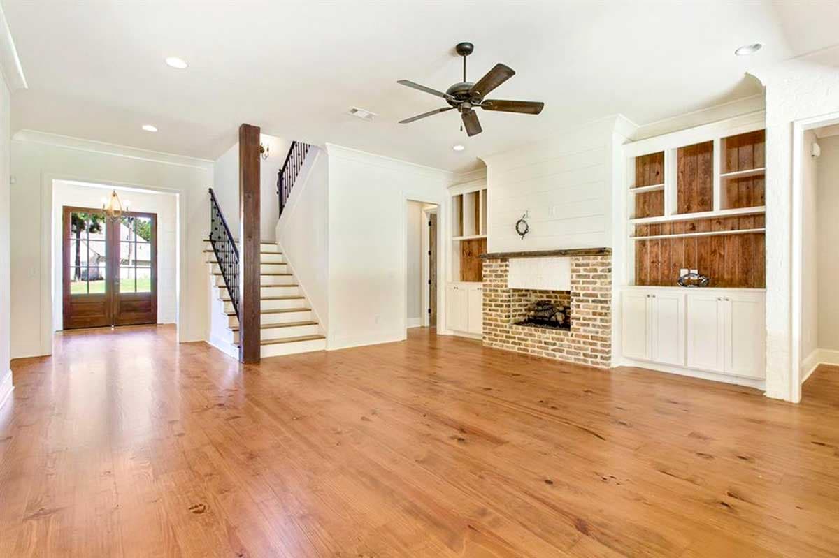 Interior view showing a living area with hardwood floors, brick fireplace, built-in shelving, and staircase.