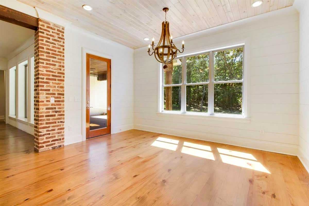 Interior rendering of a room with wood floors, brick accent wall, wood door, shiplap walls, and large window.