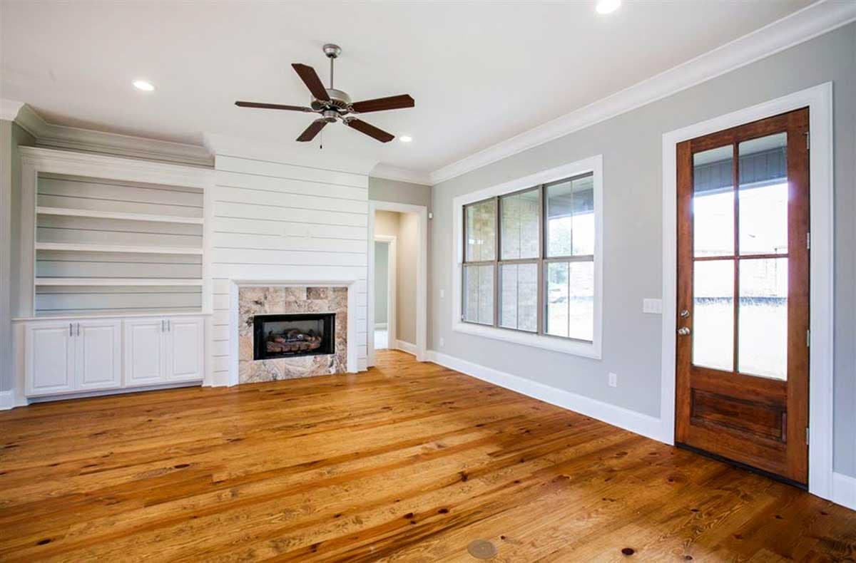 Living room with shiplap fireplace, built-in shelving, large window, wood floors, and wood door.