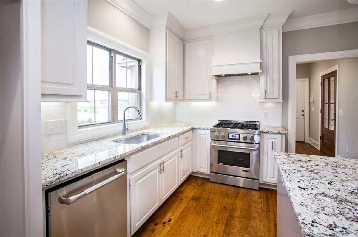 Kitchen with white cabinets, granite countertops, stainless steel appliances including a dishwasher and gas range, and a double-hung window.
