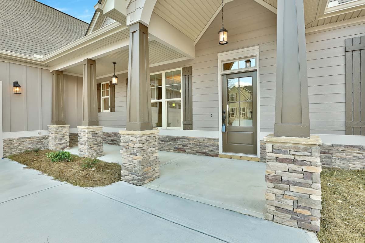 House plan exterior featuring a covered porch with stone-clad columns, board-and-batten siding, and a modern farmhouse style.