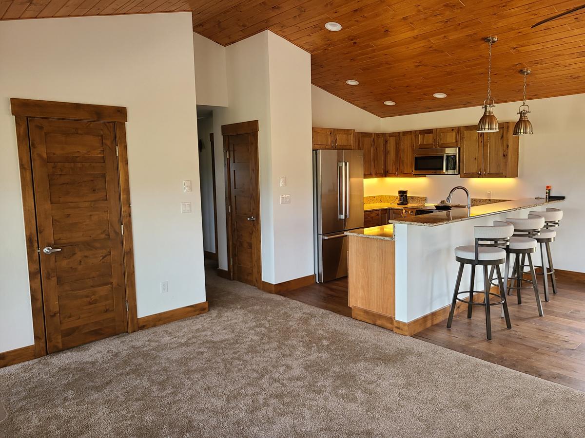 Interior view of a home with wood panel ceiling, kitchen with island and bar stools, and wood doors.