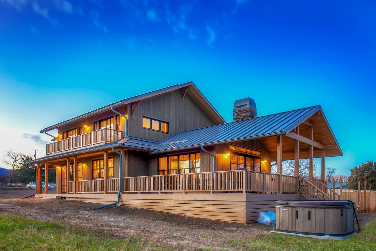 Modern Farmhouse house plan exterior with wood siding, metal roof, wraparound deck, and second-story balcony.