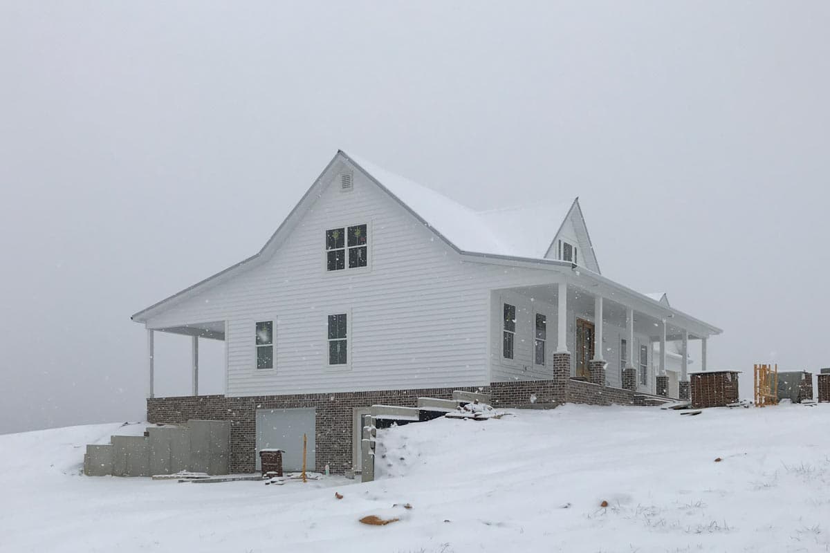 Modern farmhouse exterior: two stories, white siding, wraparound porch with brick columns, gabled rooflines, and dormers.
