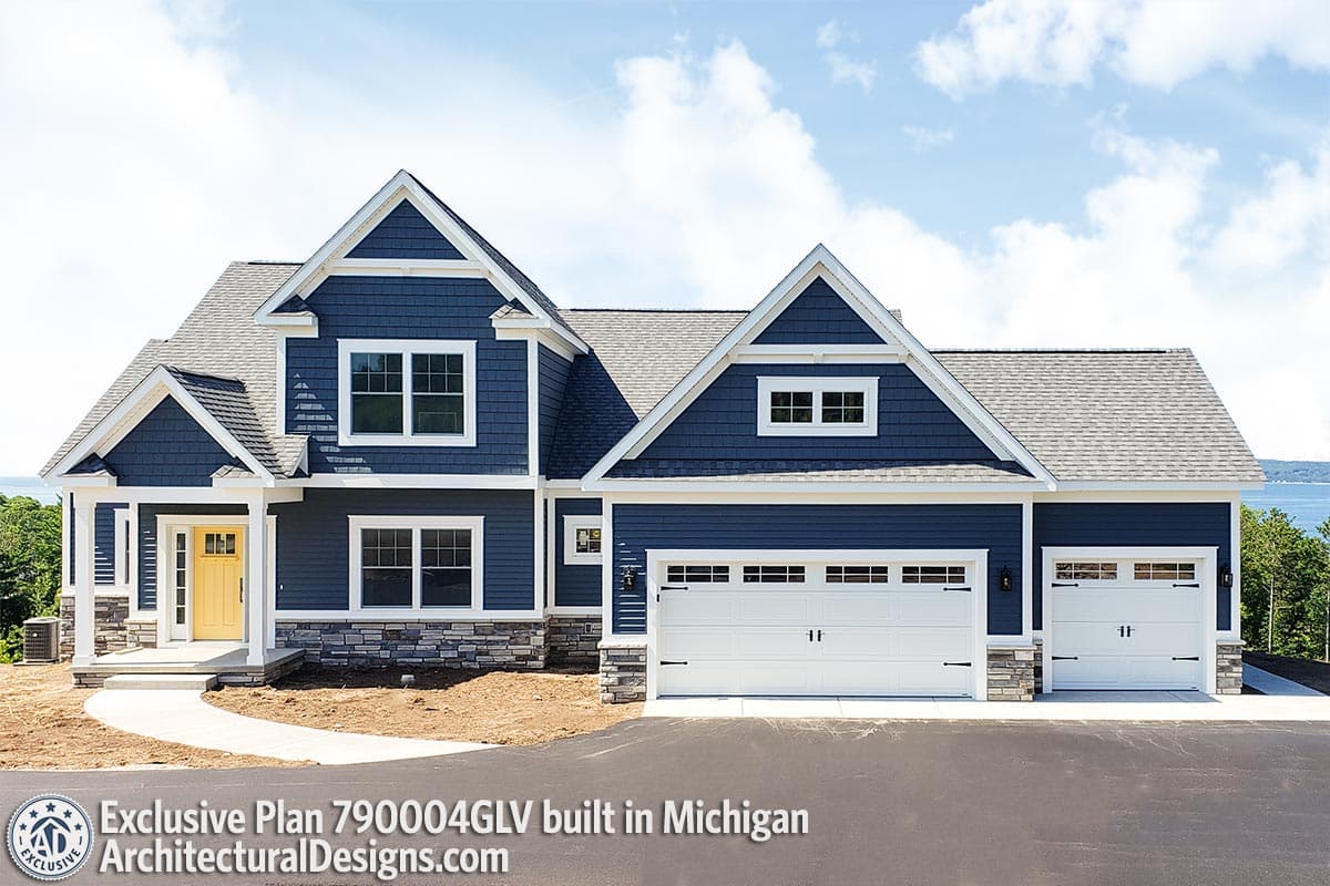 House plan exterior with blue shingle siding, stone accents, gabled dormers, covered entry, and a three-car garage.