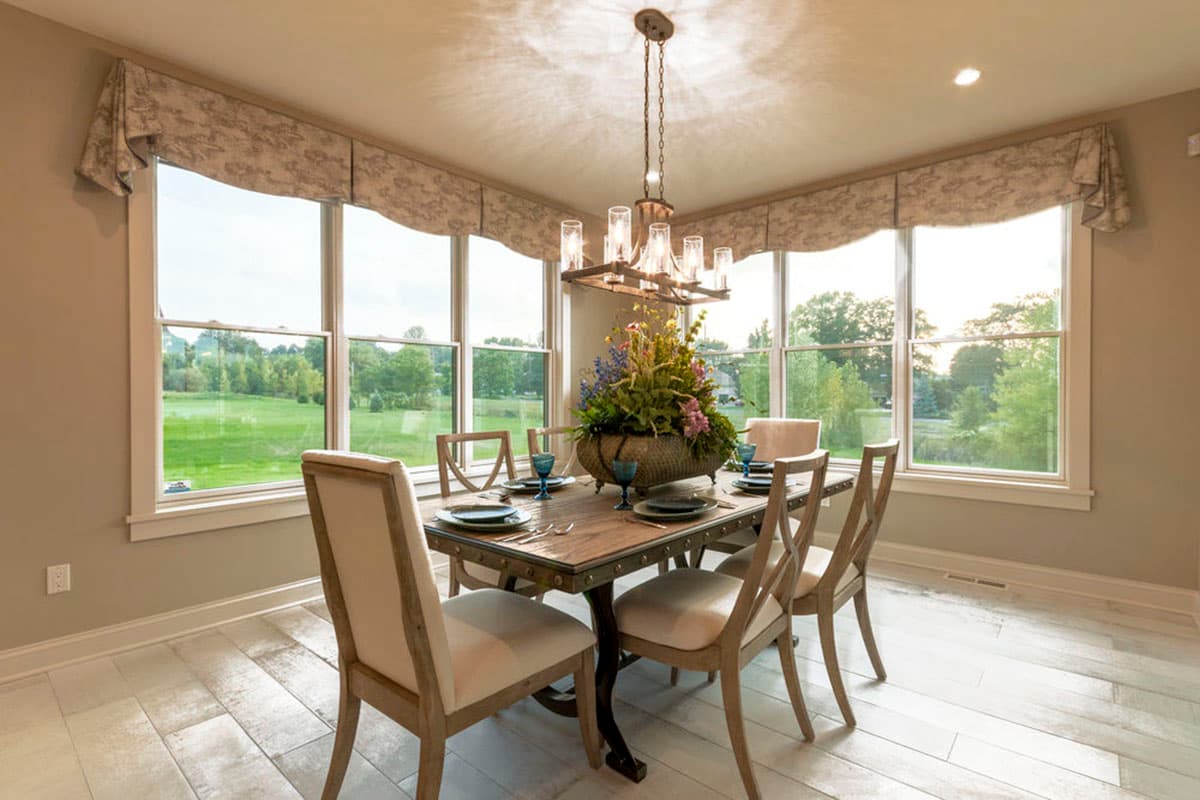 Dining room with a table and chairs, large bay windows with valances, and a chandelier.