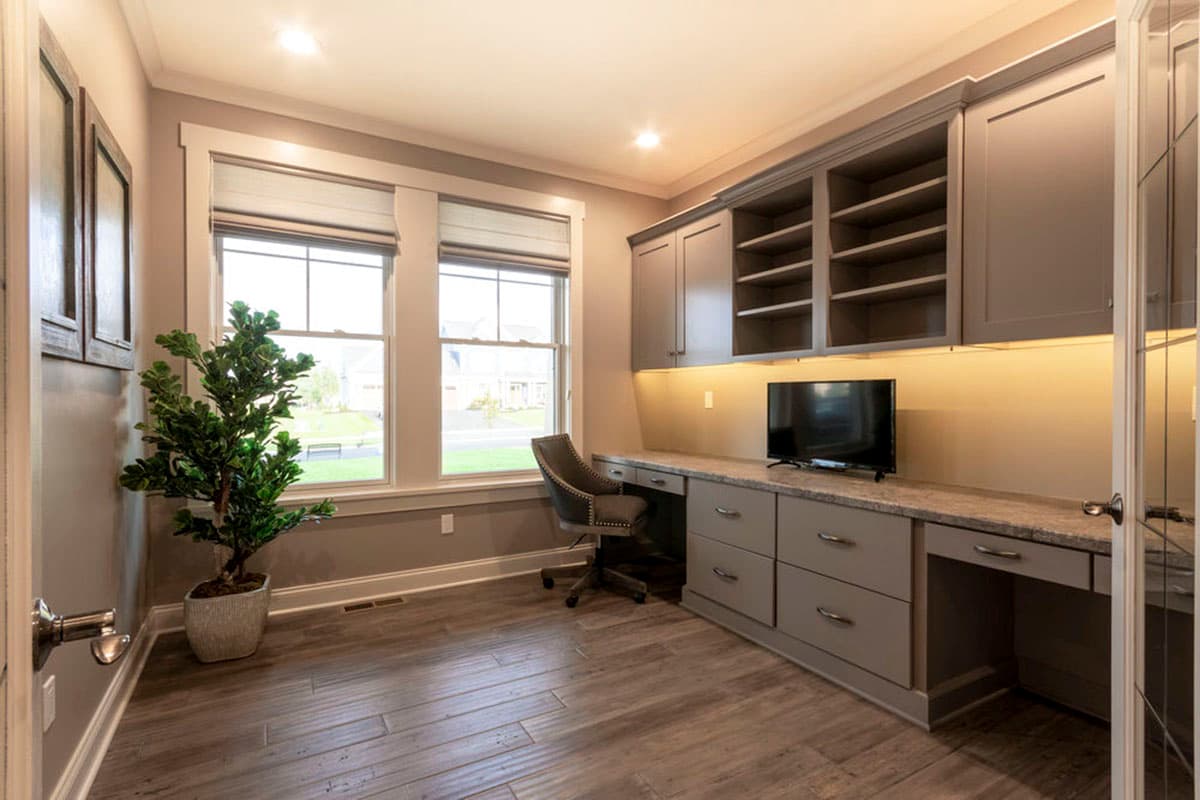 Home office with built-in cabinetry, desk, television, and double-hung windows.