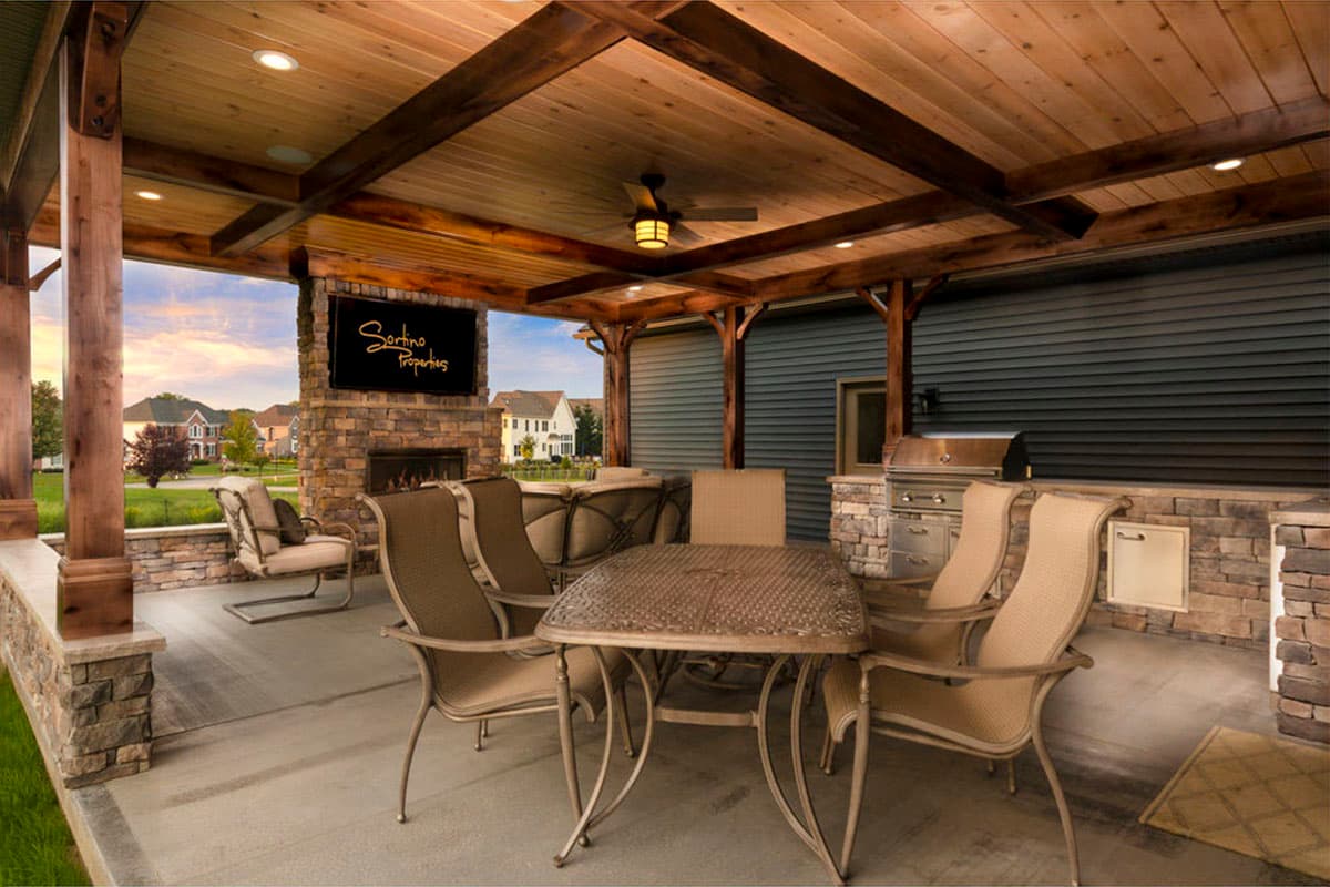 Covered patio with wood ceiling, stone fireplace with television, outdoor grill, dining table, and seating.