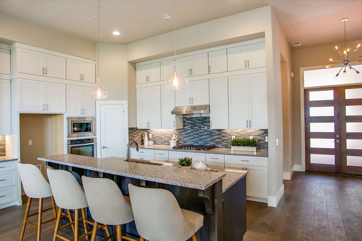 Kitchen with large island, white shaker cabinets, stainless steel appliances, mosaic tile backsplash, and natural light.