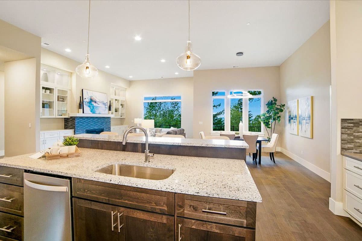 Kitchen island with sink, adjacent dining area, and living room with large windows and fireplace.