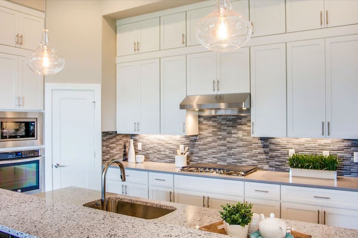 Kitchen interior with white cabinets, granite island with sink, stainless steel range hood, and decorative tile backsplash.