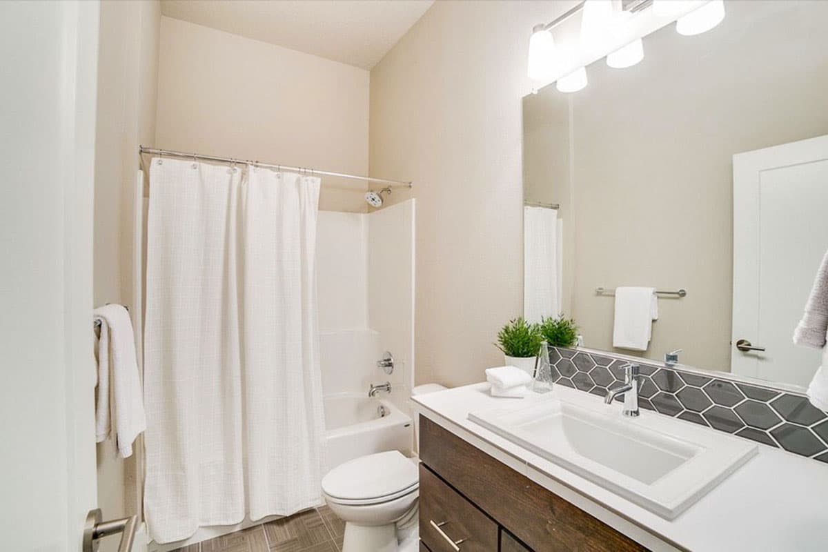 Bathroom with bathtub, shower, toilet, and vanity featuring a dark wood cabinet and hexagonal tile backsplash.