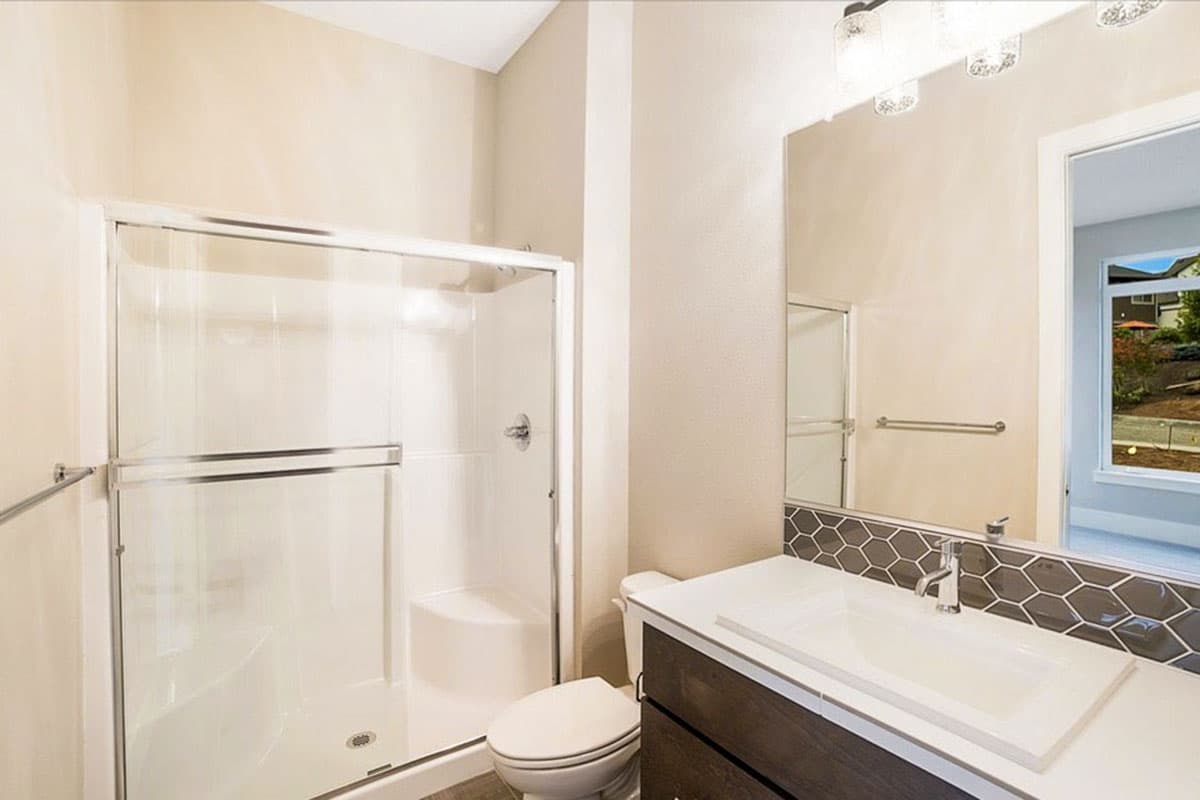 Modern bathroom with glass-enclosed shower, white vanity, and hexagonal tile backsplash.