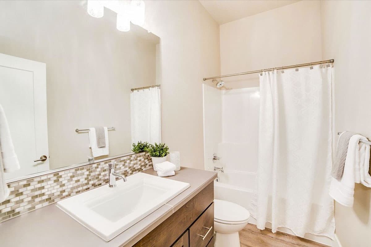 Bathroom interior with single vanity, mosaic backsplash, toilet, and bathtub with shower curtain.