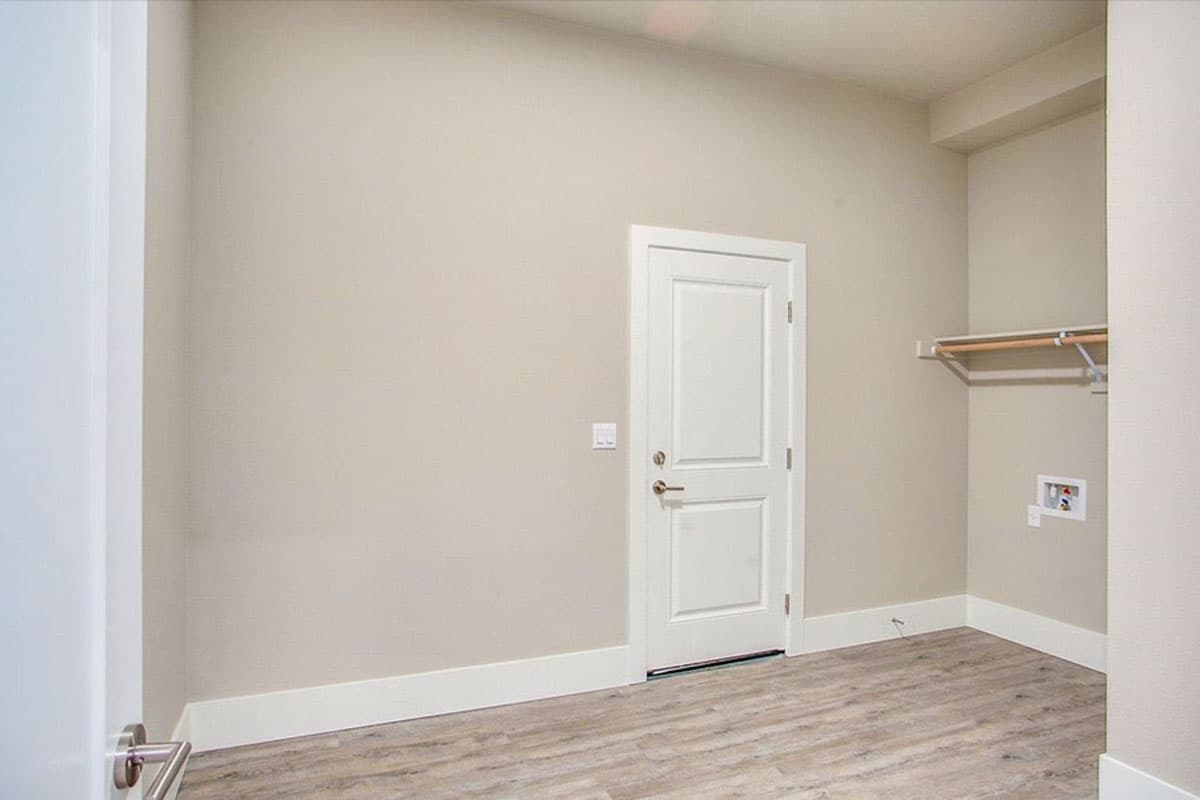 Interior view of laundry room with white door, closet rod, and utility hookups.