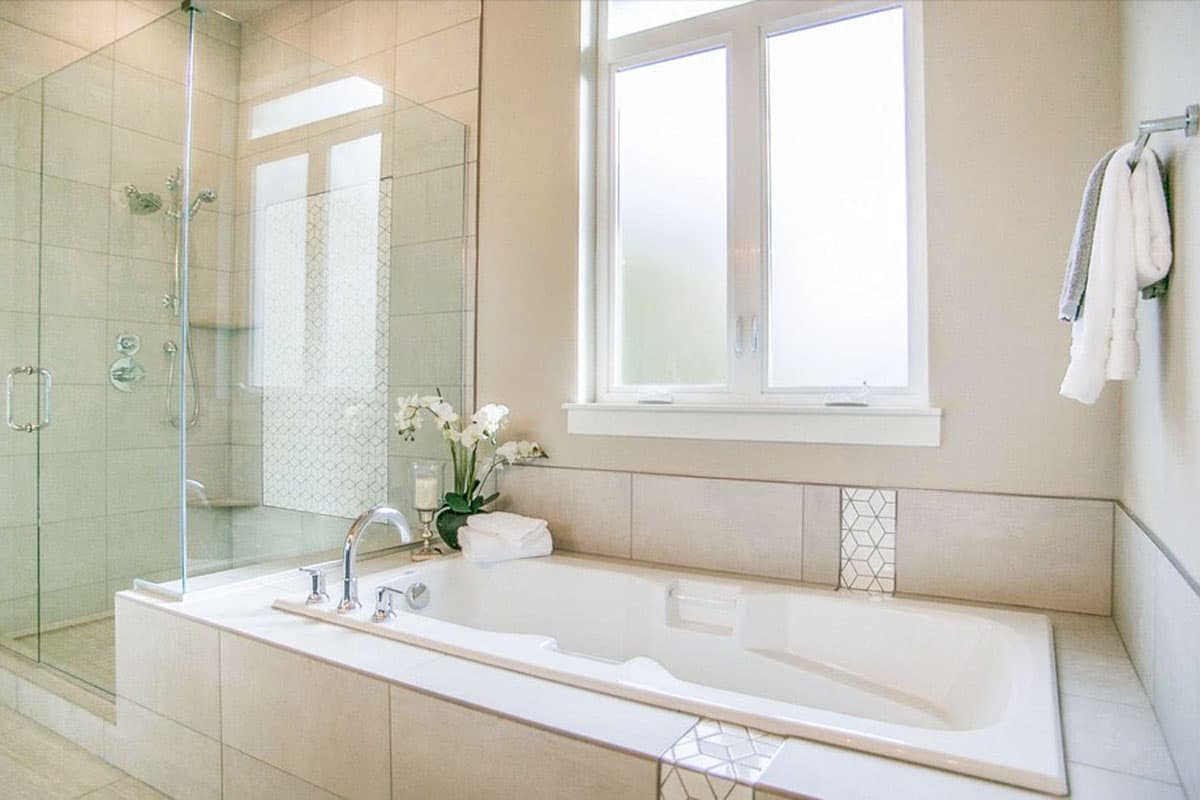 Bathroom with corner soaking tub, glass-enclosed shower with tile surround, and triple-pane window.