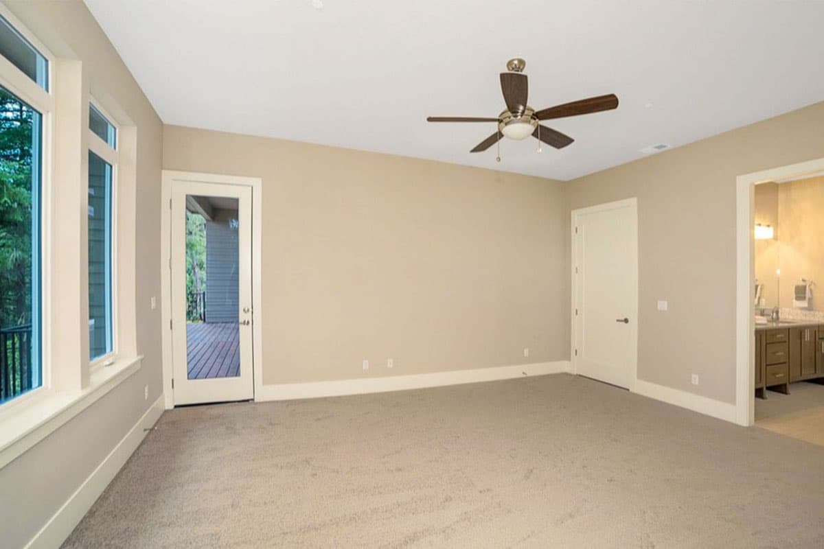 Bedroom with carpet, ceiling fan, door to deck, and doorway to en suite bathroom with double vanity.