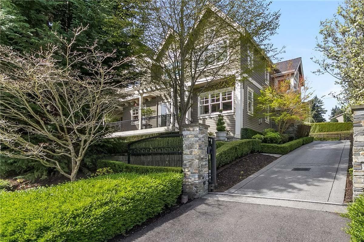 Craftsman style house exterior with gabled rooflines, covered porch with railing, and stone pillar gate.