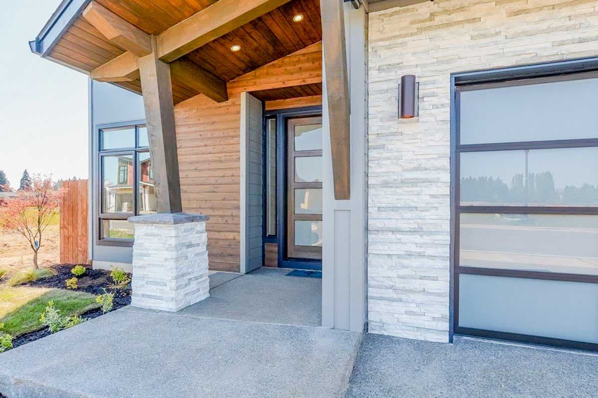 House plan exterior featuring a modern style with wood siding, stacked stone accents, a covered entry with wood ceiling, and large windows.