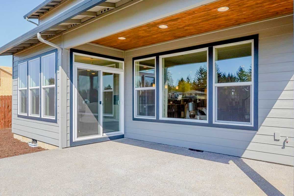 Modern house exterior with a covered patio, wood ceiling, large windows, and sliding glass door.