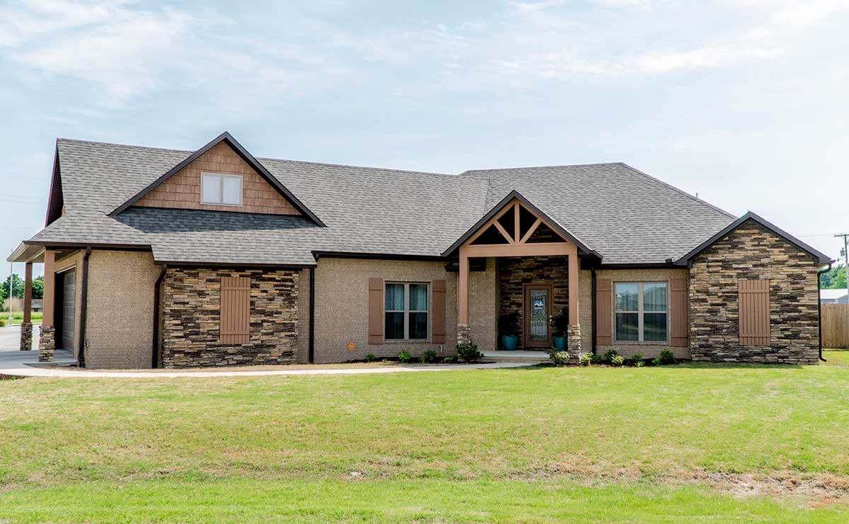 House plan exterior: One-story home with stone accents, prominent gables, covered entry with wooden beams, and attached garage.