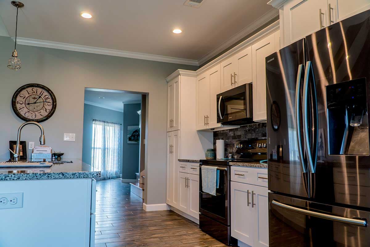 Kitchen interior with white cabinets, microwave, oven, refrigerator, granite countertop, and a doorway to another room.