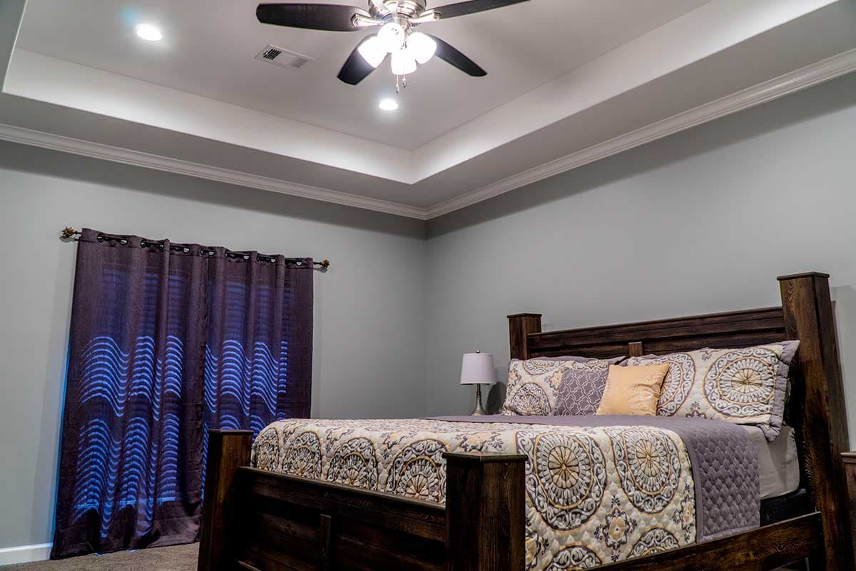Bedroom interior with coffered ceiling, ceiling fan, king bed with patterned bedding, and dark wood furniture.