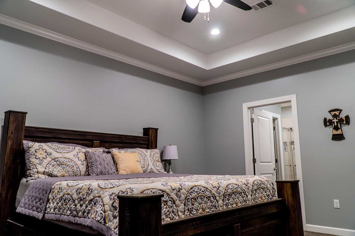 Primary bedroom with a tiered ceiling featuring crown molding, a dark wood bed, and decorative wall cross.